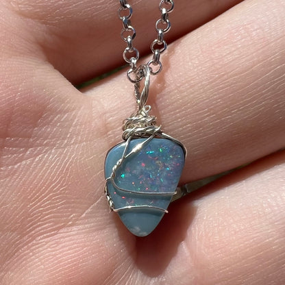 Close-up macro view of N5 dark opal doublet pendant in sterling silver wire wrapped pendant, shown in sunlight held in a hand.