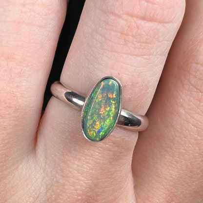 Close-up macro view of a sterling silver N5 dark Australian opal solitaire women's ring worn on a finger.  The opal has green, orange, and yellow play of color.