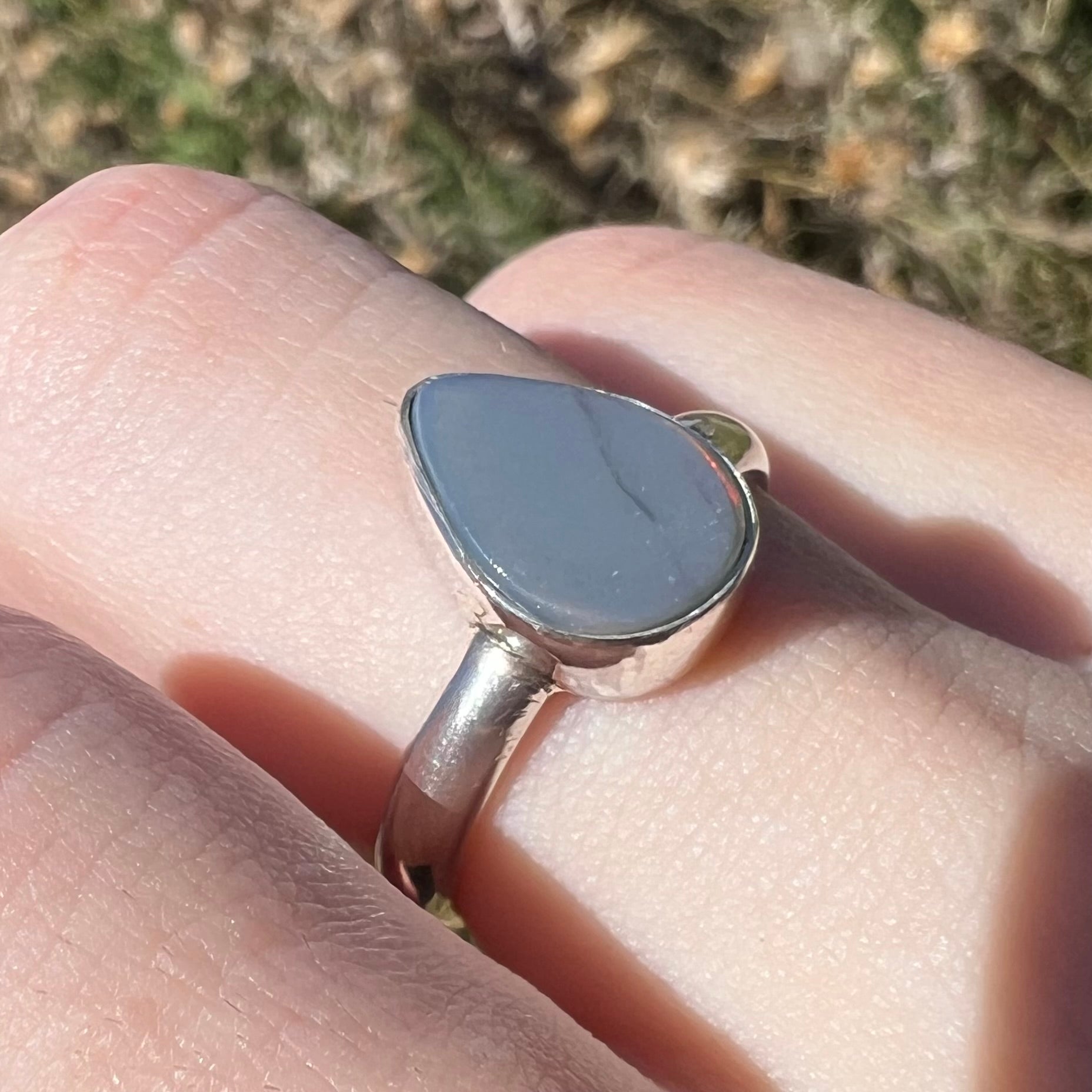 Close-up of a sterling silver Lightning Ridge opal ring with an N6 dark body tone, viewed on a finger in sunlight.  No play of color is present.