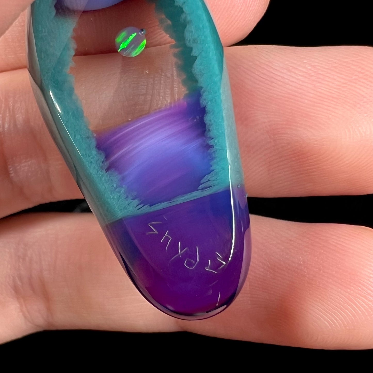 Close-up of a signature, "Snyder", etched into the back of a purple and teal glass and lab-opal pendant by artist, Nathan Snyder.