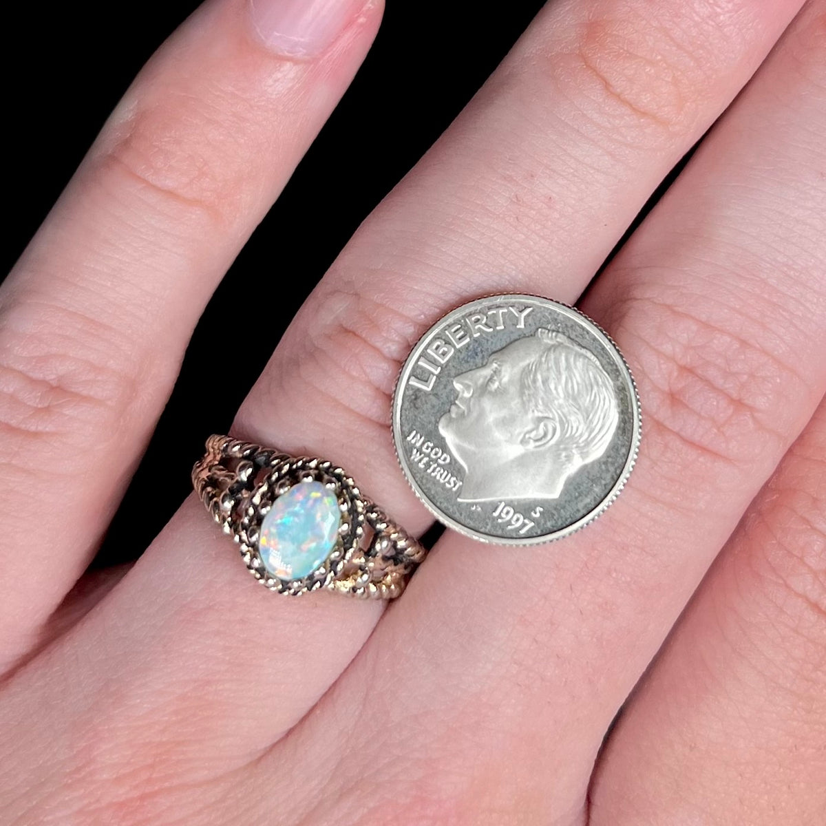 Close-up of a natural Australian opal solitaire brass ring worn on hand next to US dime coin