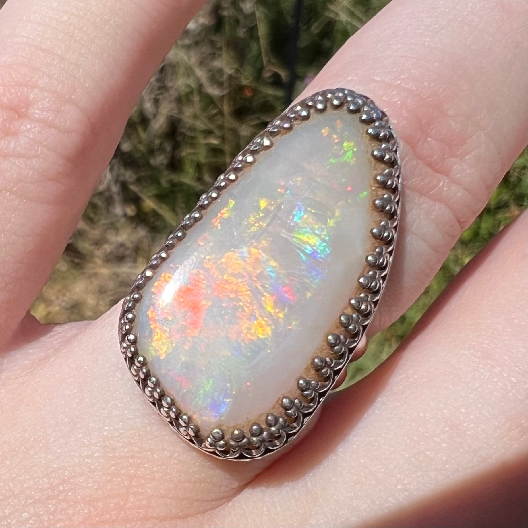 Close-up of a sterling silver natural Australian opal ring in sunlight.  The opal has brilliant red and orange multicolor fire.