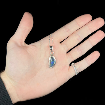 Hand holding a natural black opal necklace in sterling silver under LED studio lights.