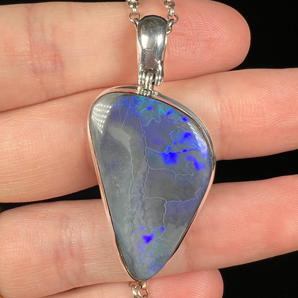 Close-up of natural black opal pendant in sterling silver, held in a hand
