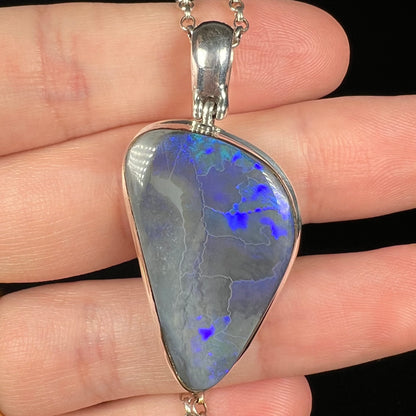 Close-up of natural black opal pendant in sterling silver, held in a hand