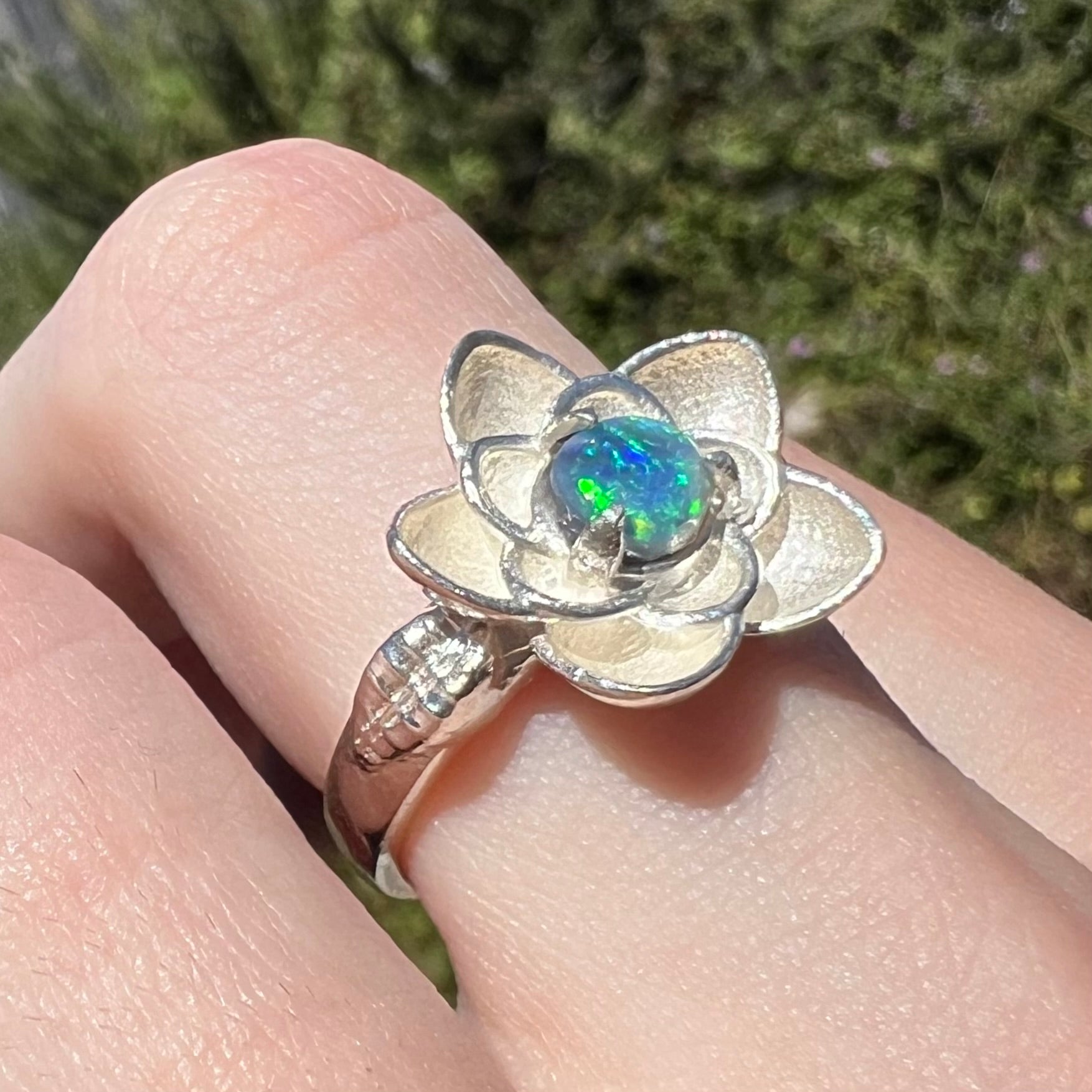 Natural black opal flower design ring in sterling silver, worn on finger in sunlight