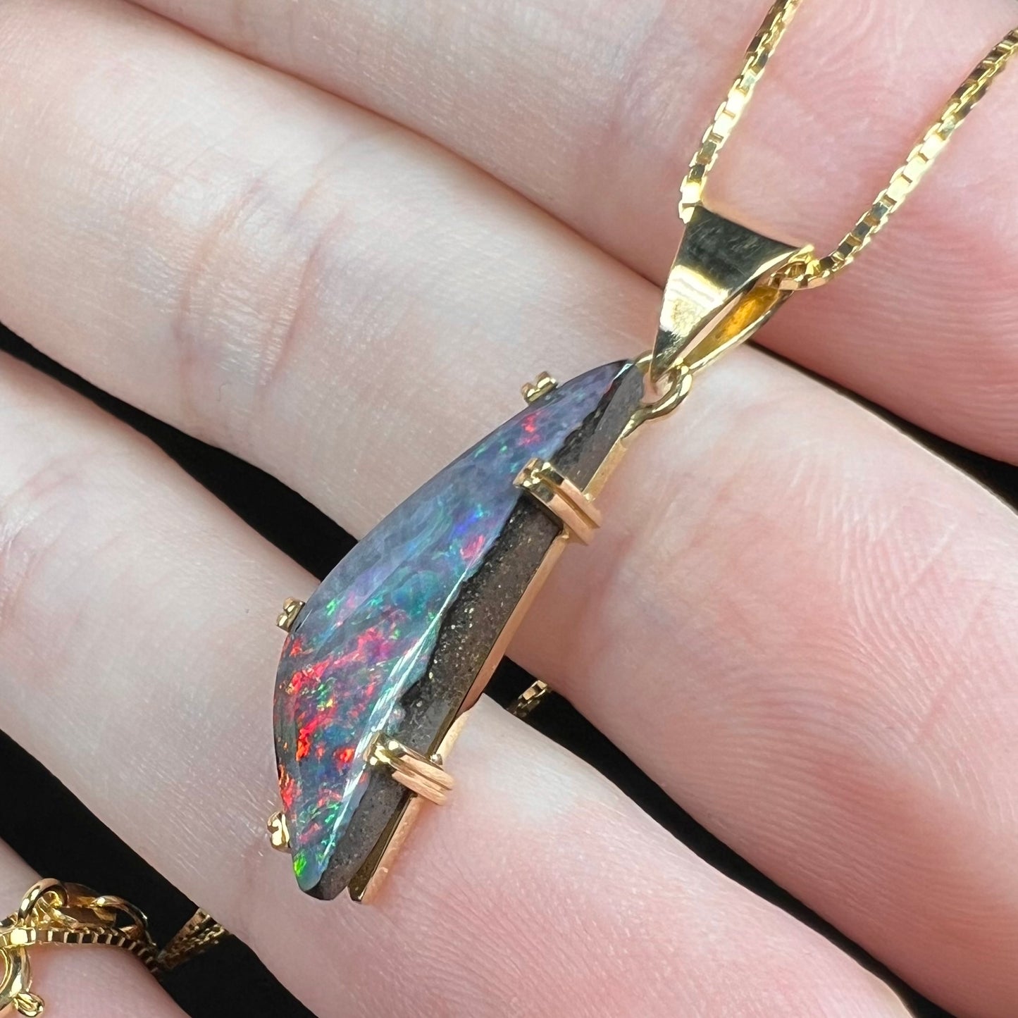 Natural Australian boulder opal pendant in 18k gold shown from side view in hand, ironstone matrix visible