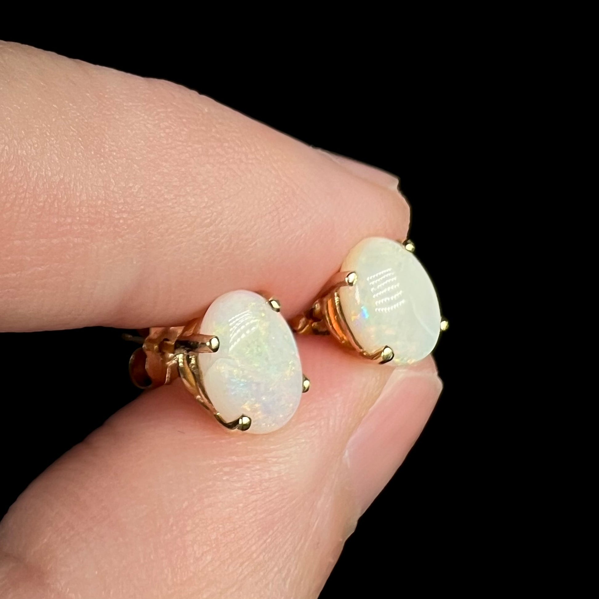 Natural opal earrings in gold shown from angle between fingers