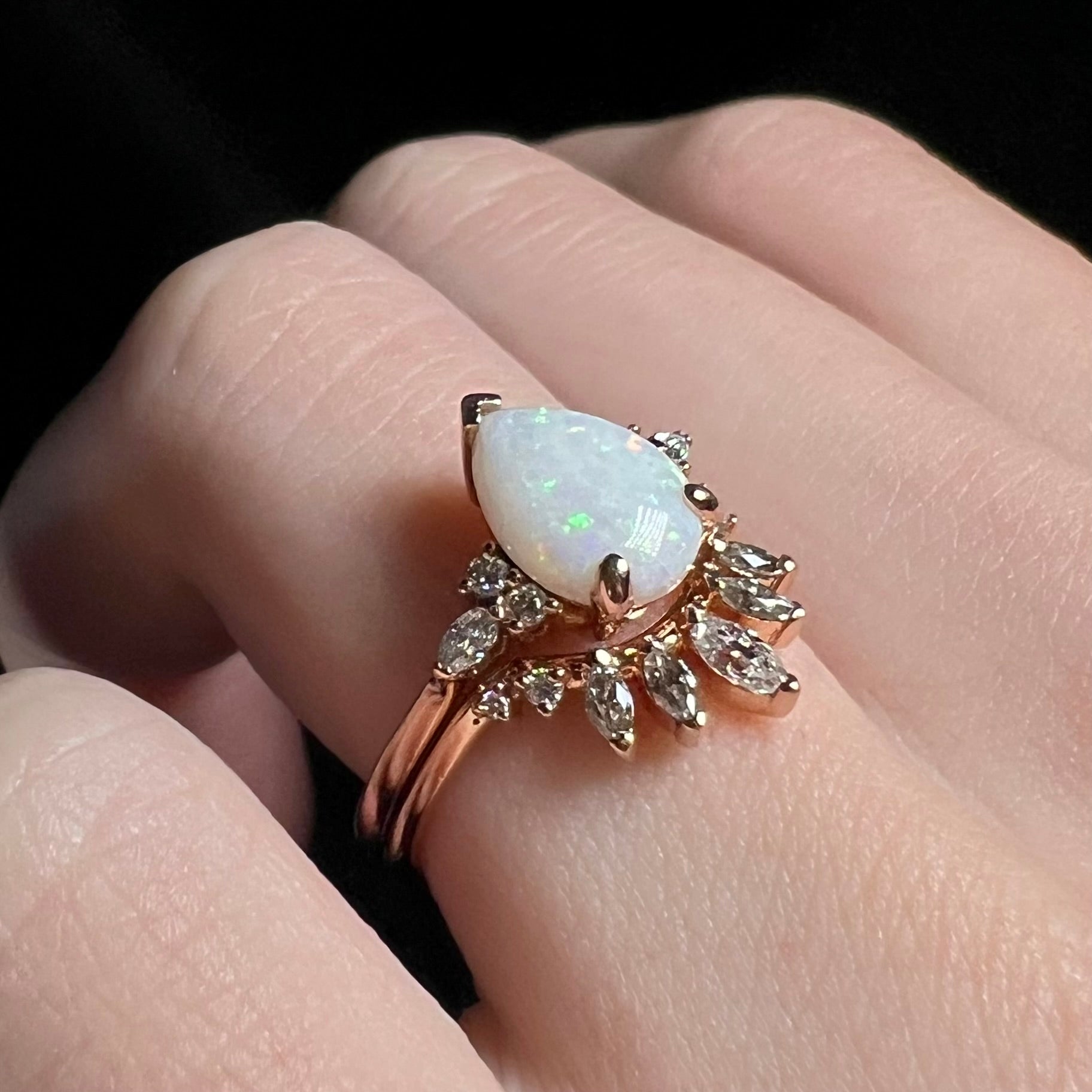 Close-up of natural opal and moissanite engagement ring set in 14k rose gold, worn on hand