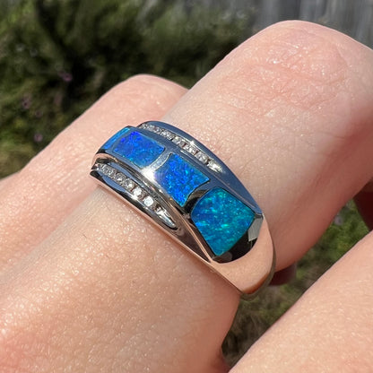 Macro view of 14k white gold inlay ring featuring natural Australian opal inlay, enhanced by black epoxy to give blue appearance, worn on finger and viewed from angle in sunlight