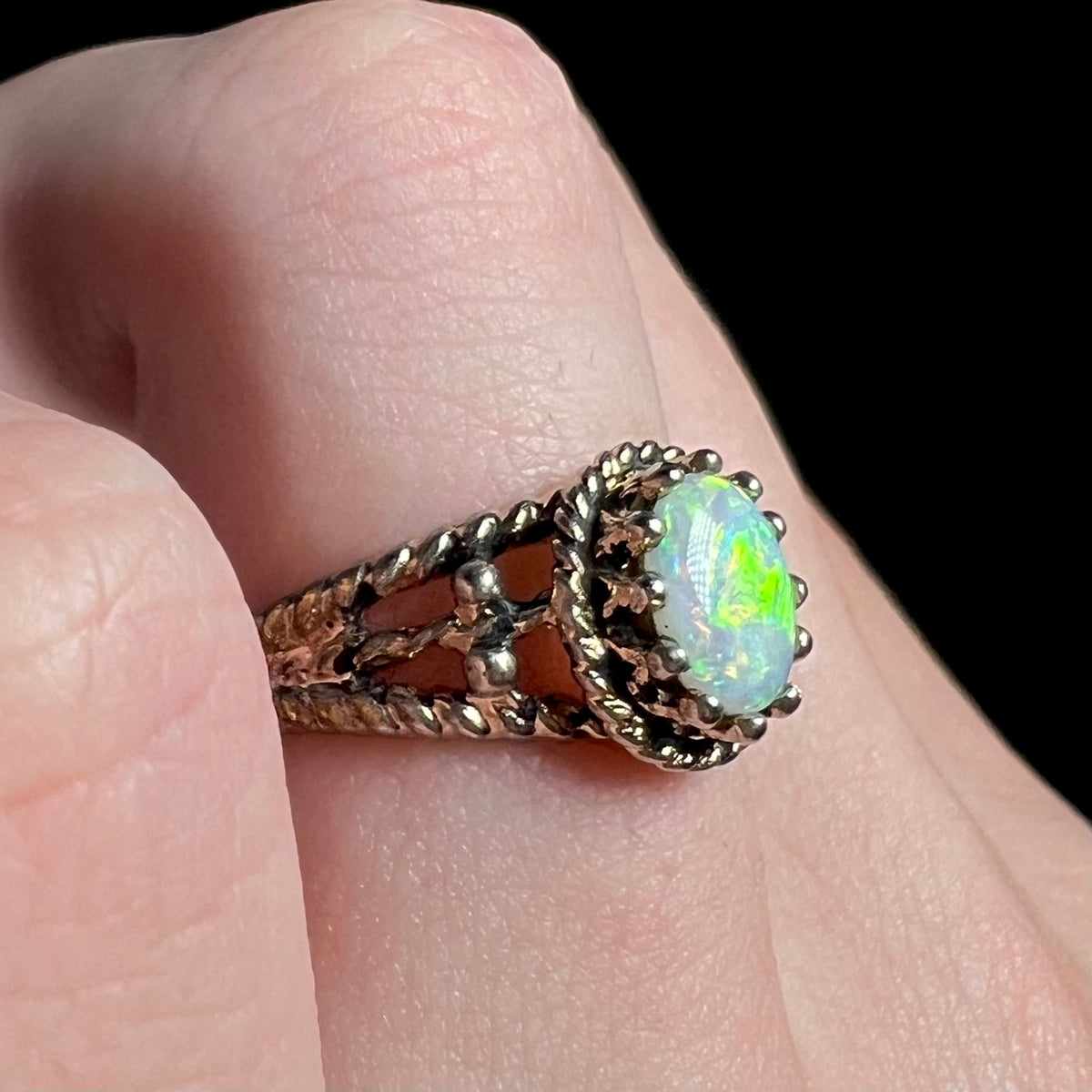 Brass solitaire ring set with natural Australian opal showing bright green flash, worn on finger and shown close-up from angle