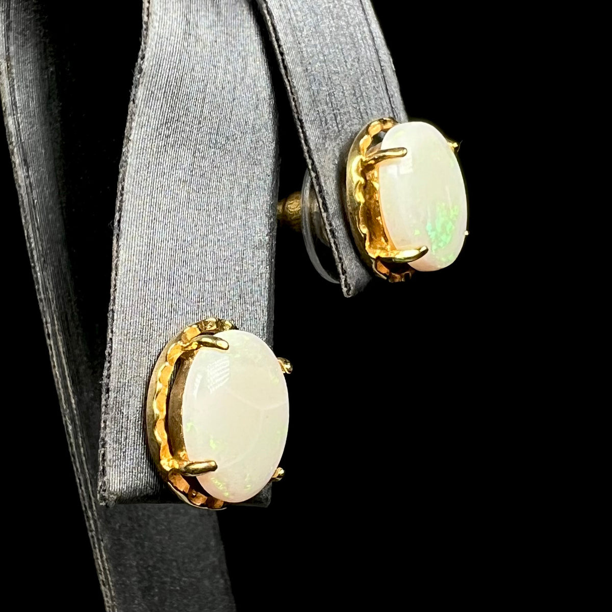 Oval shaped natural opal stud earrings in gold-plated costume base metal, shown on earring display