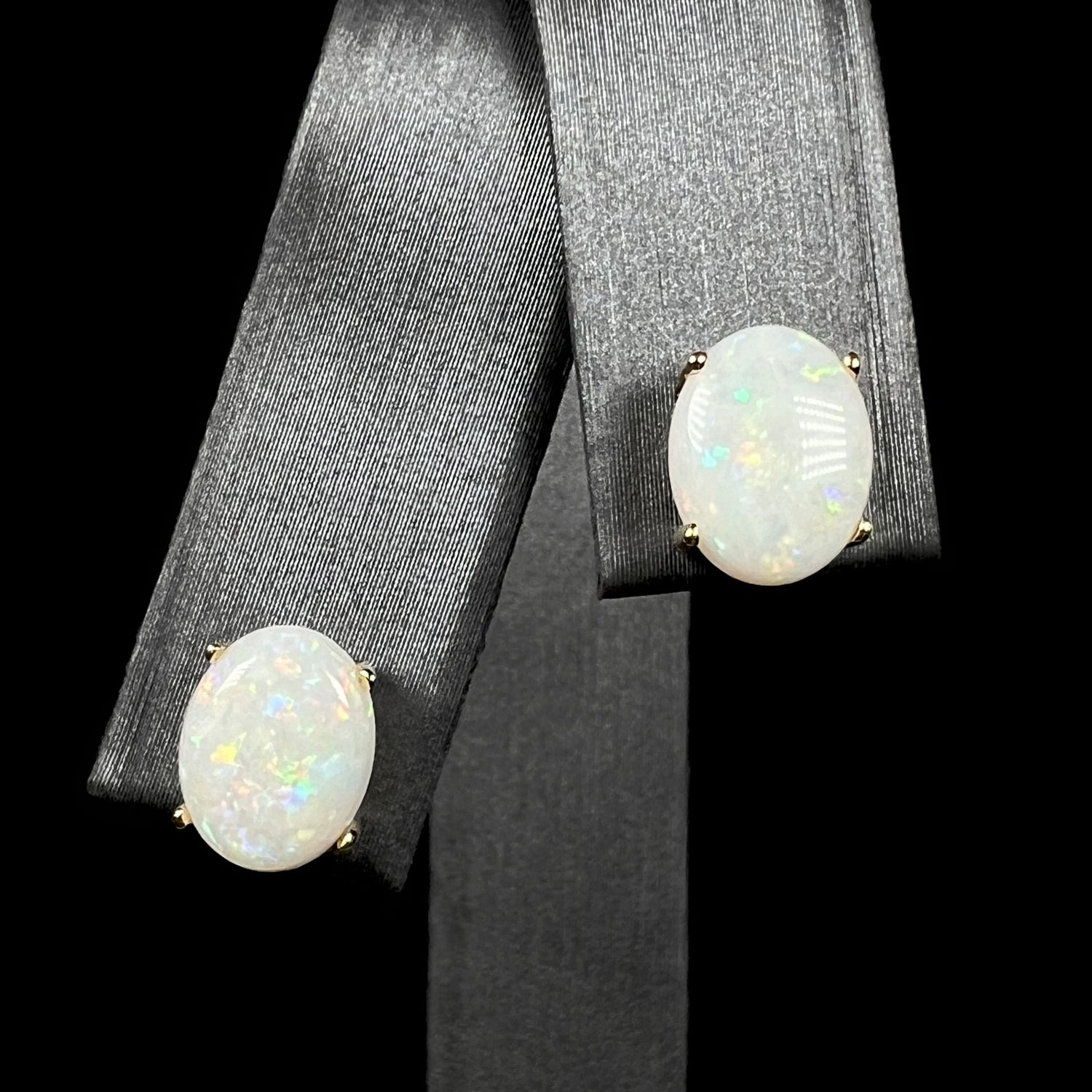 A close-up of natural opal stud earrings in 14k yellow gold on a black display, showing subtle color play.