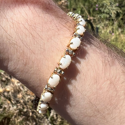 Side close-up view of a natural white Australian opal and diamond bracelet around a wrist in sunlight.