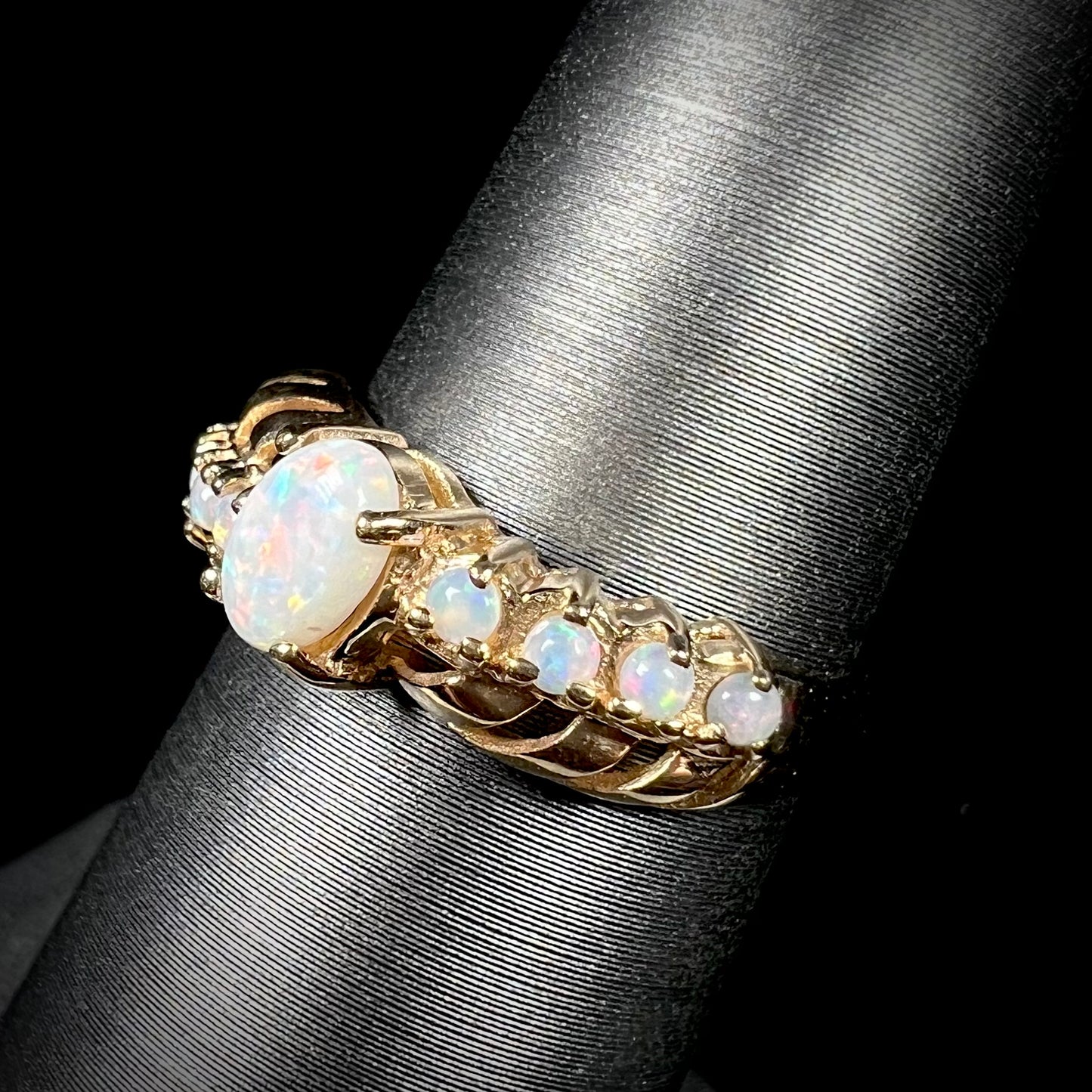 A natural white opal crisscross ring in yellow gold, shown on a ring display from an angle.