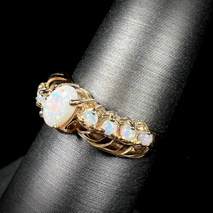 A natural white opal crisscross ring in yellow gold, shown on a ring display from an angle.