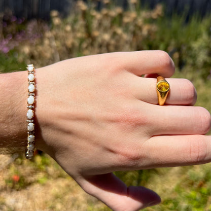 Hand wearing a 10k gold natural white opal and diamond tennis bracelet on wrist in sunlight along with a 24k gold yellow sapphire ring on finger.