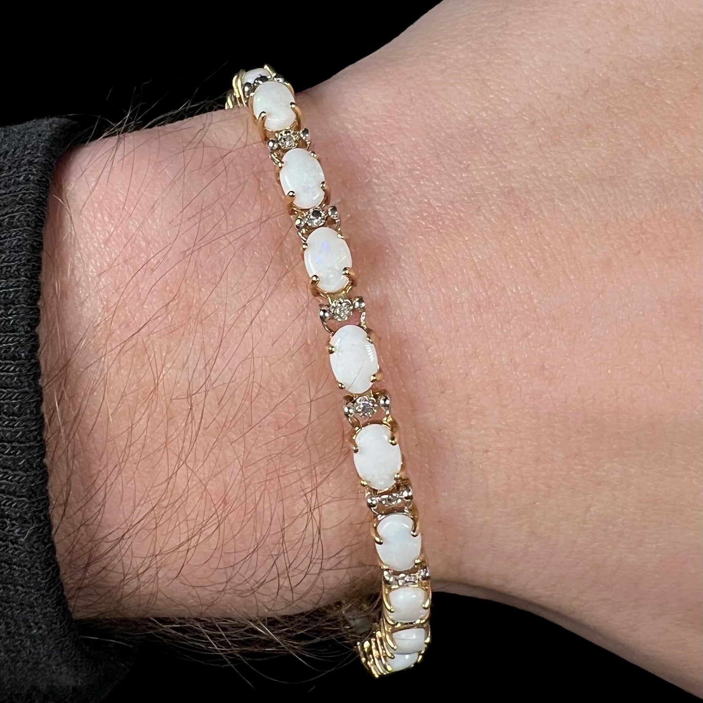 A 10k yellow gold natural white opal and diamond-accented tennis bracelet worn around a wrist shown close-up.