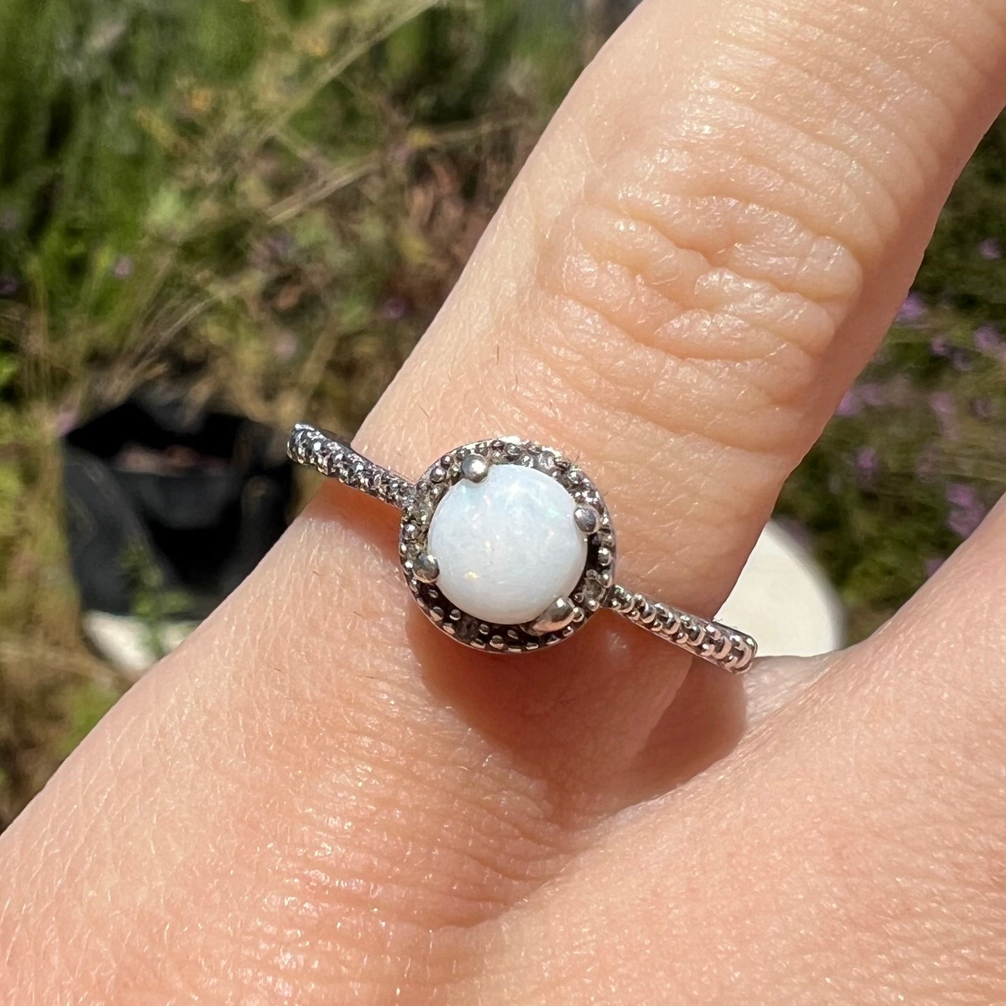 Close-up front view of a natural white opal ring in sterling silver, worn on a pinkie finger in the sunlight.