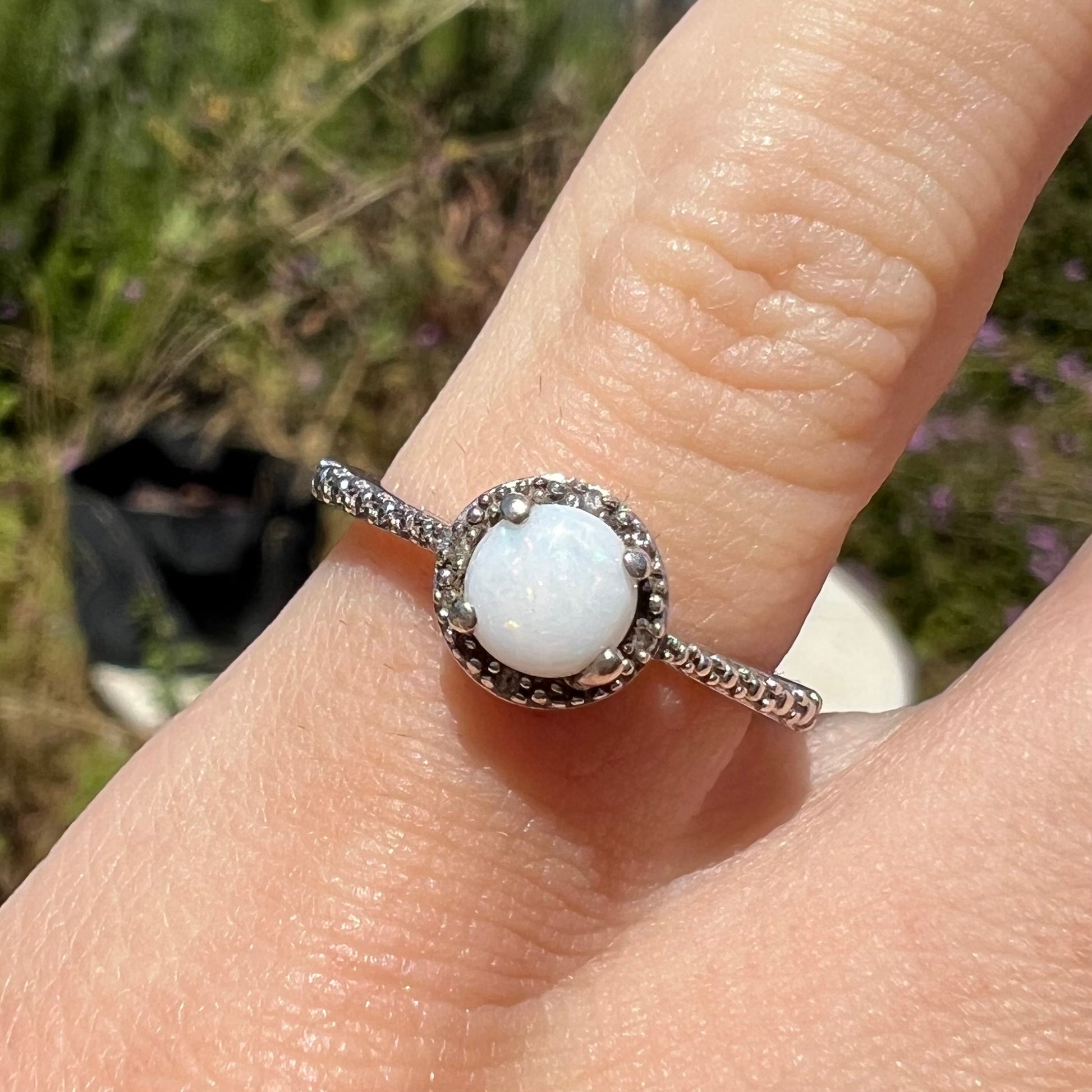 Close-up front view of a natural white opal ring in sterling silver, worn on a pinkie finger in the sunlight.