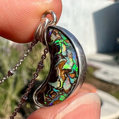 A sterling silver necklace set with a natural Koroit boulder opal shaped like a crescent moon.