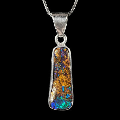 A sterling silver necklace bezel set with a natural Australian boulder opal stone.  The stone shines colors of blue, green, and purple.