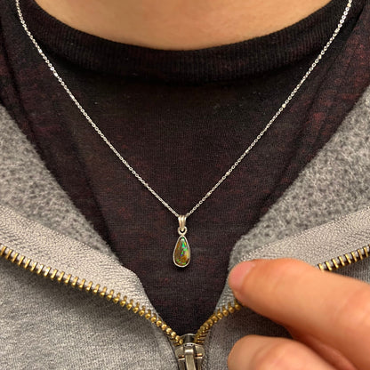 A natural, pear shaped Australian boulder opal with blue, purple, and green colors bezel set into a sterling silver necklace.