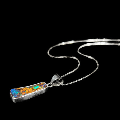 A sterling silver necklace bezel set with a natural Australian boulder opal stone.  The stone shines colors of blue, green, and purple.