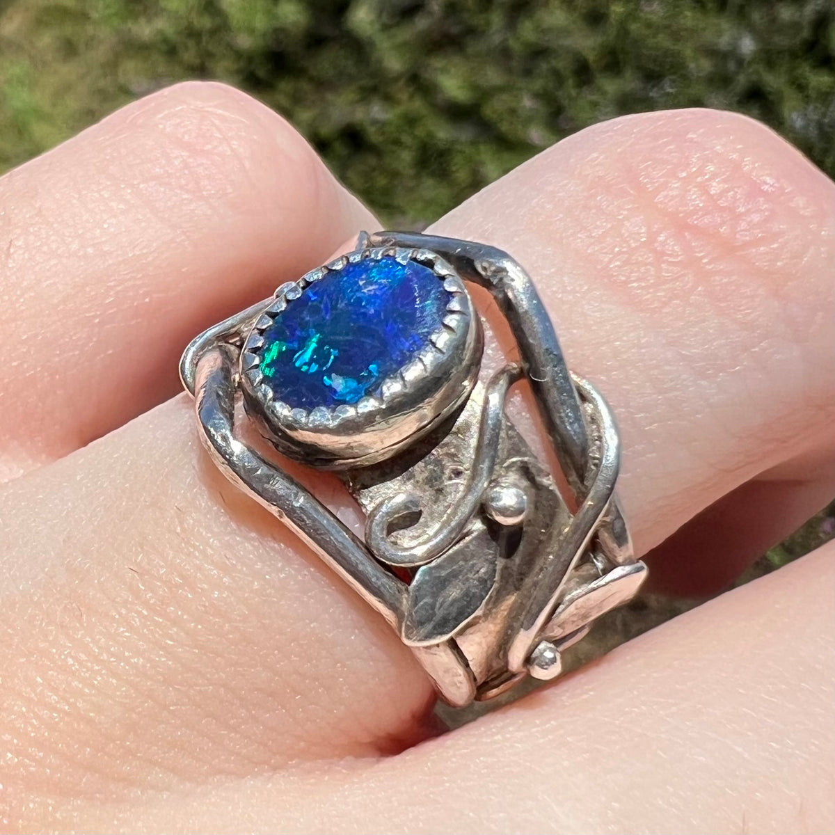 Close-up of handmade black opal doublet ring in sterling silver with nature-inspired motif, worn on finger under direct sunlight