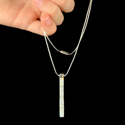 A Navajo inlay pendant being dangled in a hand, showing the opal inlay side.