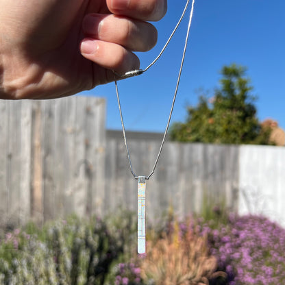 A Navajo inlay pendant being dangled outdoors, showing the opal inlay side.