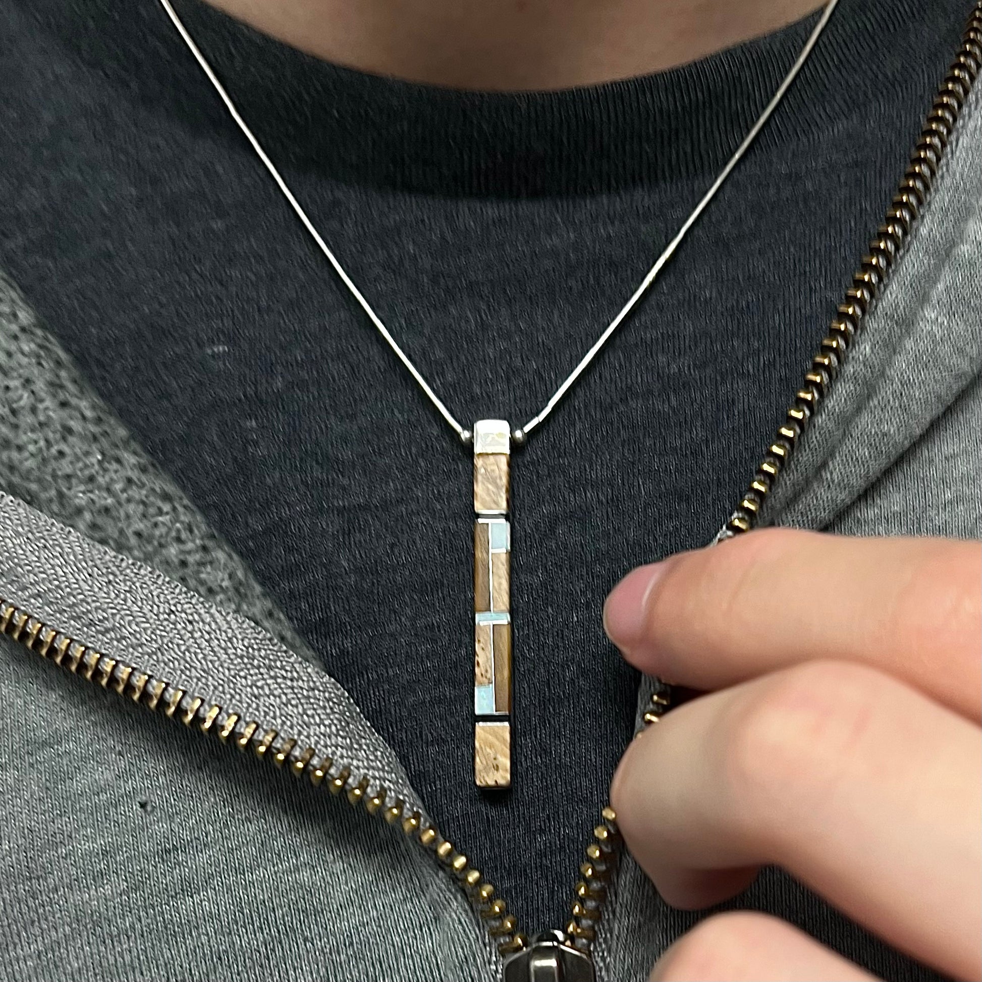 A Navajo inlay pendant worn around the neck on a black T-shirt, showing the jasper inlay side.