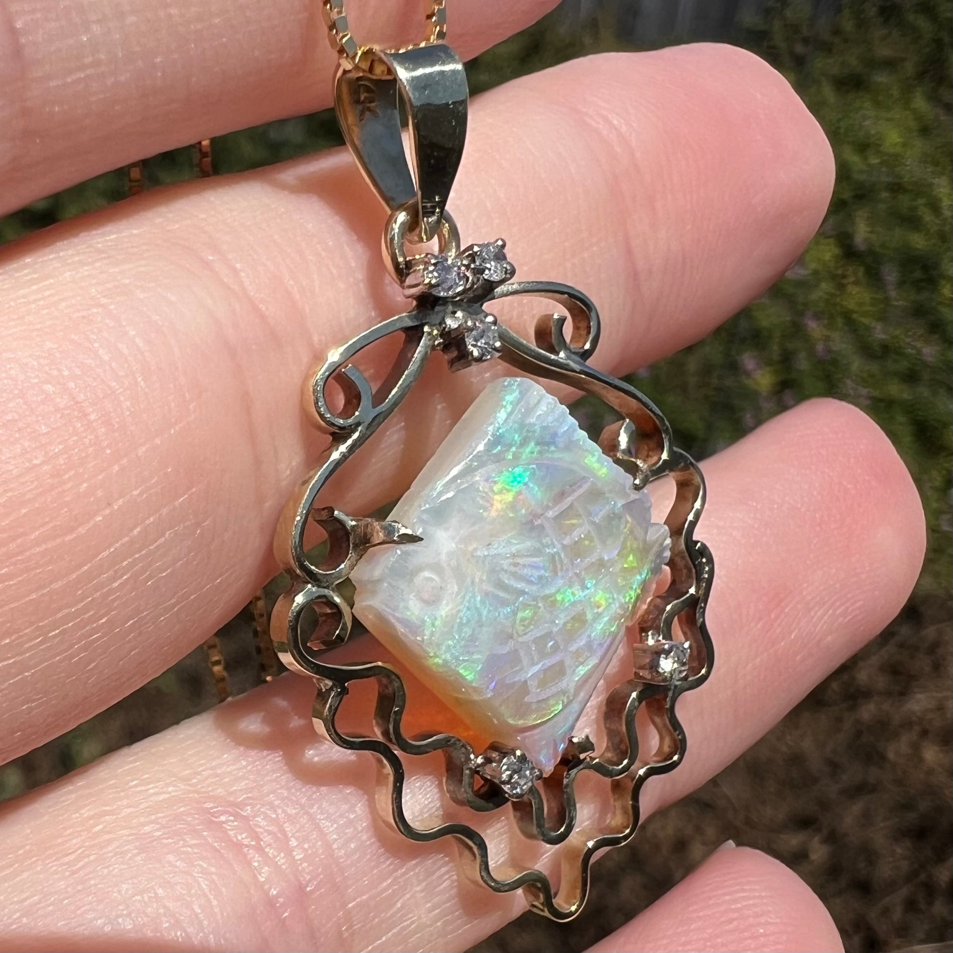 Close-up sunlit view of ocean-inspired carved opal fish pendant in gold with diamond bubble accents