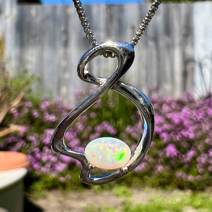 A ladies' sterling silver necklace set with an oval cabochon cut natural white crystal opal with green fire.