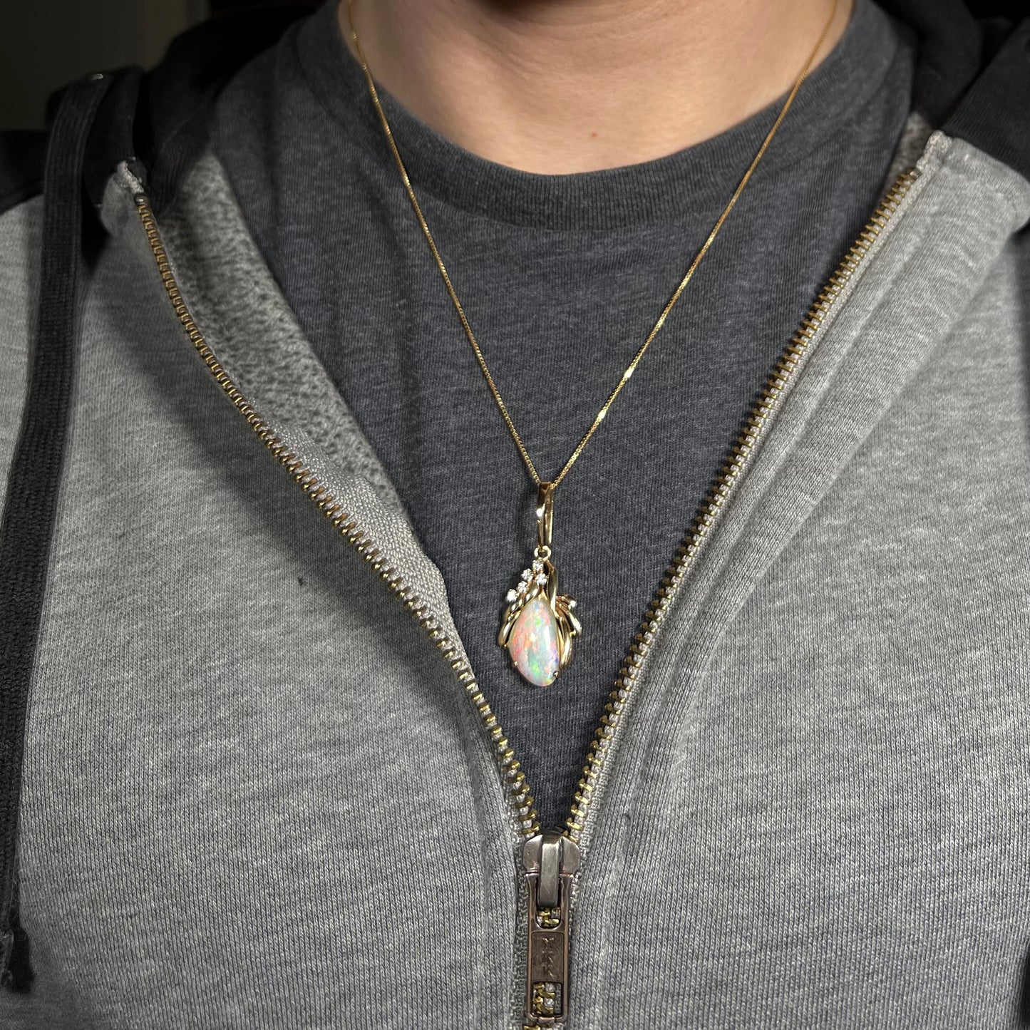An old-fashioned 14k gold Australian shell opal and diamond necklace, worn around a person's neck against a dark shirt under a gray hoodie.