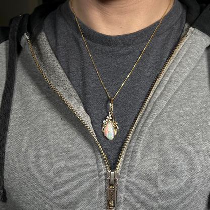 An old-fashioned 14k gold Australian shell opal and diamond necklace, worn around a person's neck against a dark shirt under a gray hoodie.