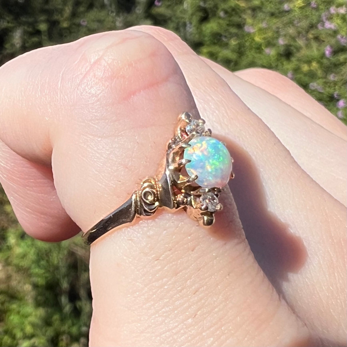 Close-up sunlit view of an opal and Old European Cut diamond ring worn on pinky finger