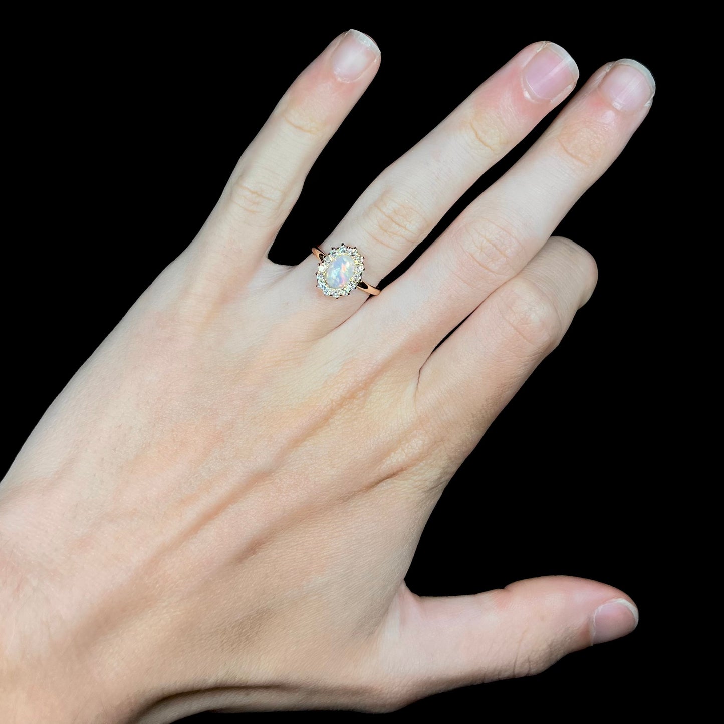 An antique opal and diamond engagement ring on a hand.  The opal is surrounded by a halo of Euro Cut diamonds.