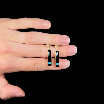 A pair of onxy opal inlay dangle earrings held in a hand, shown from the front.