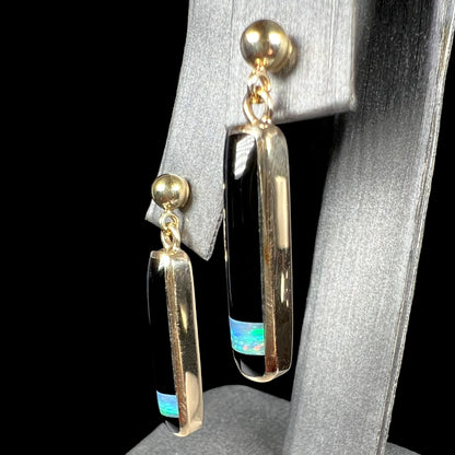 Angled view of a pair of onyx and opal inlay drop earrings made from yellow gold.