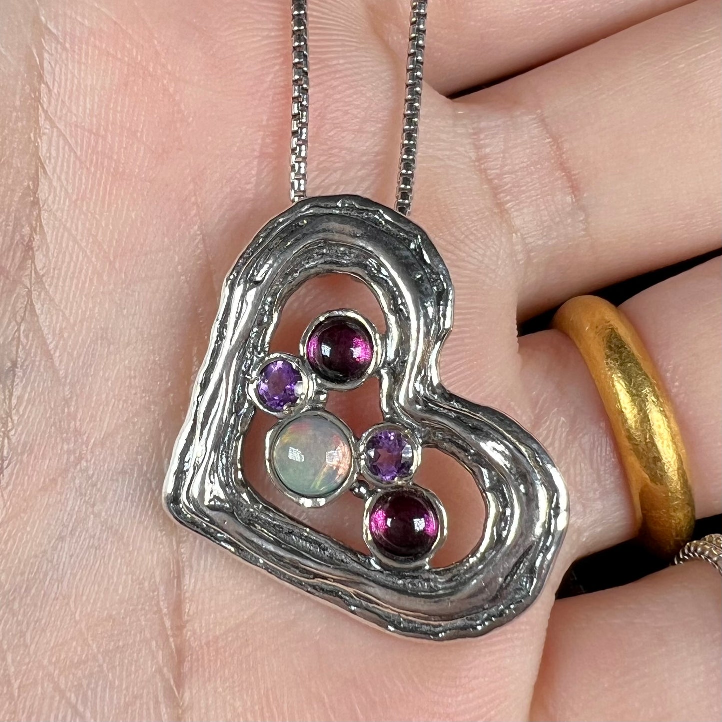 A sterling silver heart necklace set with a round Ethiopoian opal, two amethysts, and two rhodolite garnets.