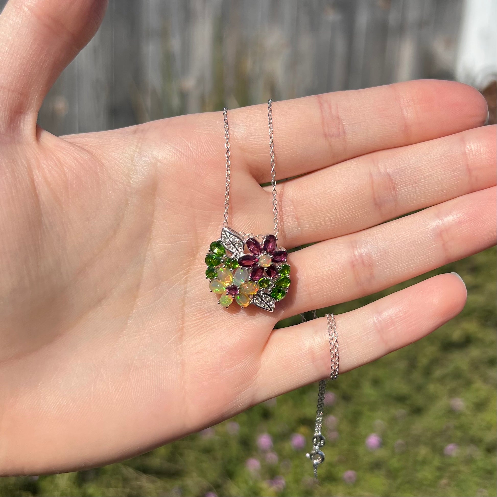 A sterling silver opal and garnet flower necklace held in a hand in sunlight.