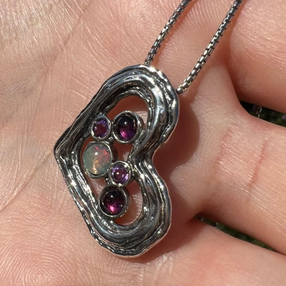 A sterling silver heart necklace set with a round Ethiopoian opal, two amethysts, and two rhodolite garnets.