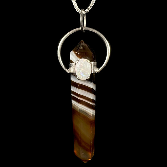 An opal and sardonyx crystal pendulum pendant shown from the front against a black background.