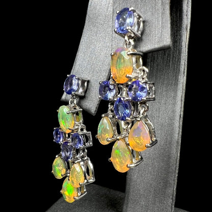 A pair of dangling sterling silver Ethiopian opal and tanzanite chandelier earrings, shown at an angle.