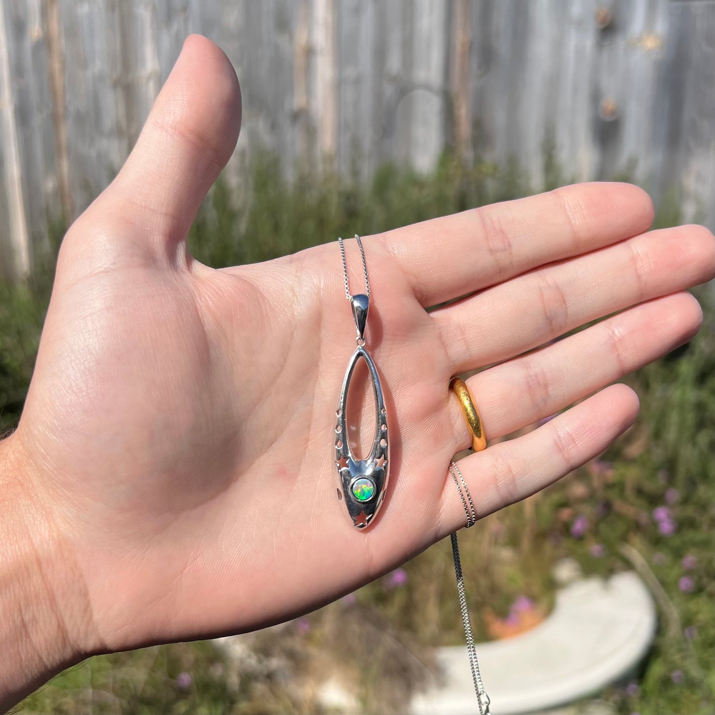 A sterling silver and opal doublet ballerina shoe necklace shown in a hand outside in the sunlight.