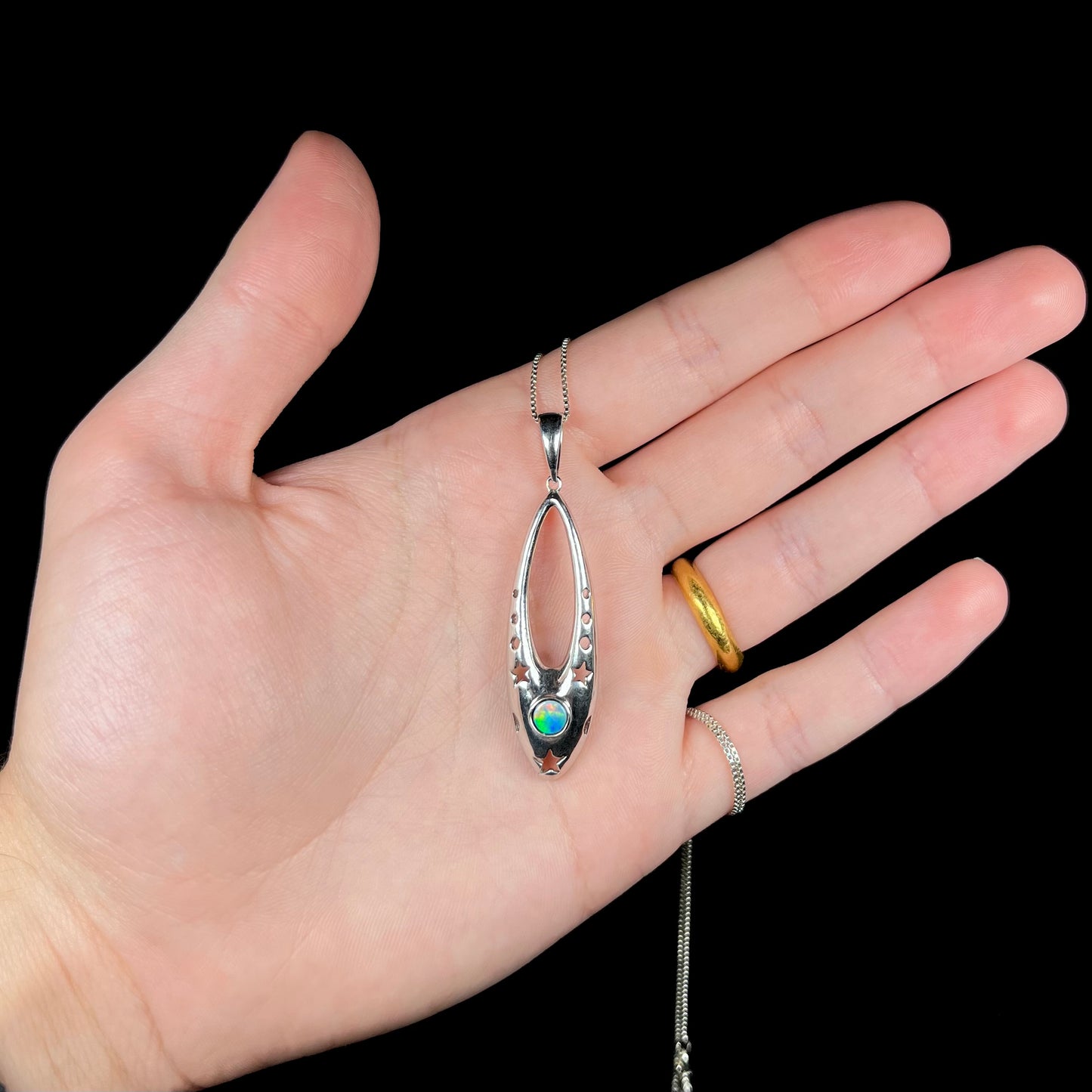 A sterling silver and opal doublet ballerina shoe necklace held in a hand against a black background.