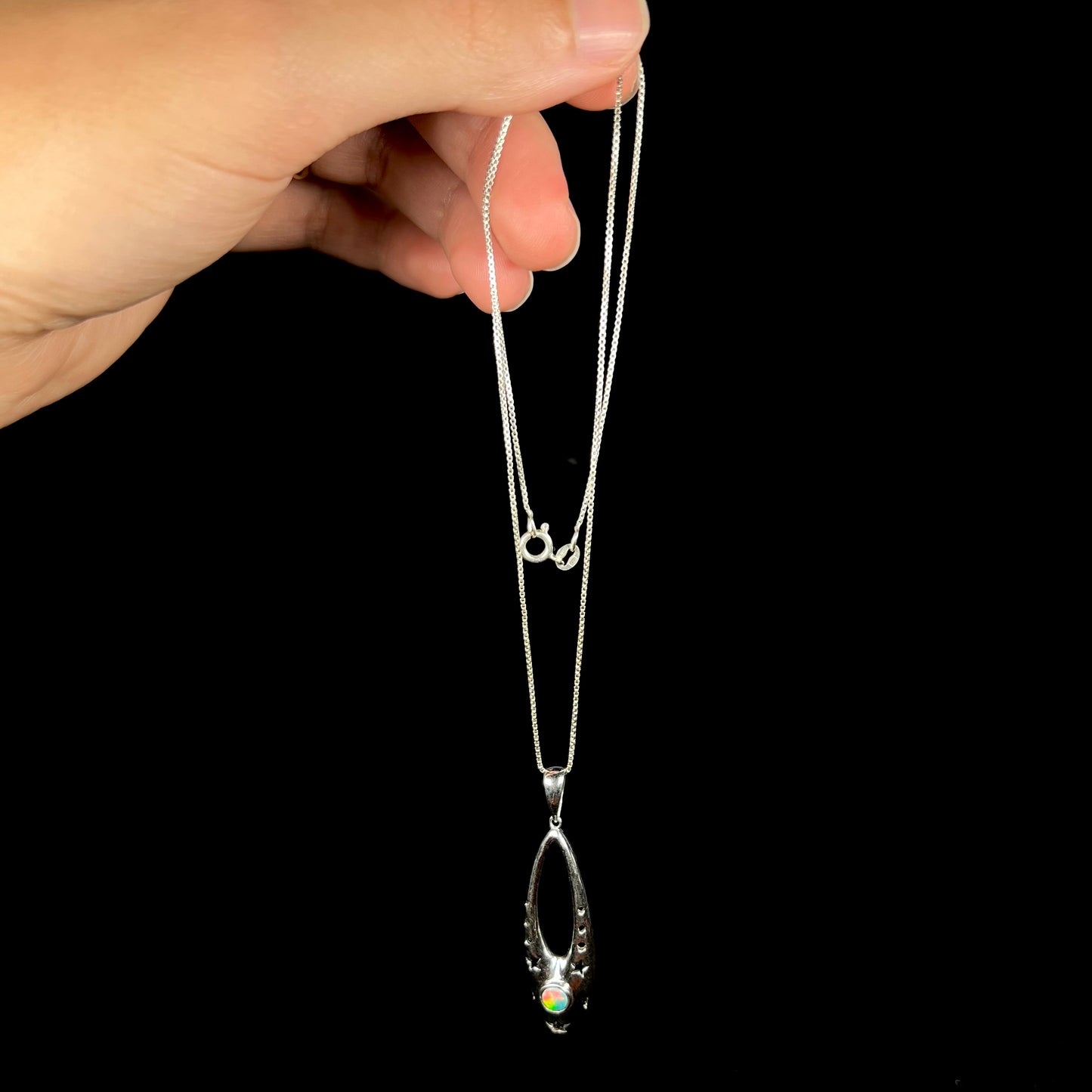 A sterling silver ballerina shoe necklace with a colorful opal, dangled by its chain from a hand.