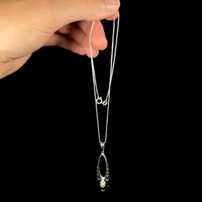 A sterling silver ballerina shoe necklace with a colorful opal, dangled by its chain from a hand.
