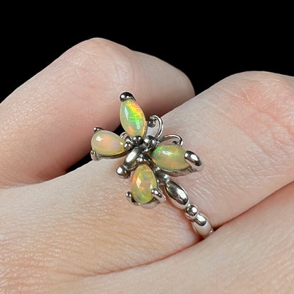 A sterling silver Ethiopian opal butterfly ring shown close-up at an angle on a finger against a black background.